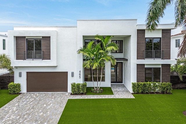 contemporary home featuring a balcony, a garage, decorative driveway, stucco siding, and a front yard