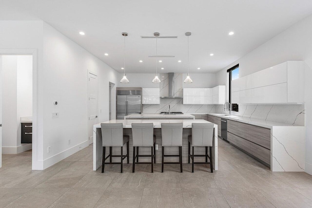 kitchen with appliances with stainless steel finishes, wall chimney range hood, a spacious island, hanging light fixtures, and white cabinets