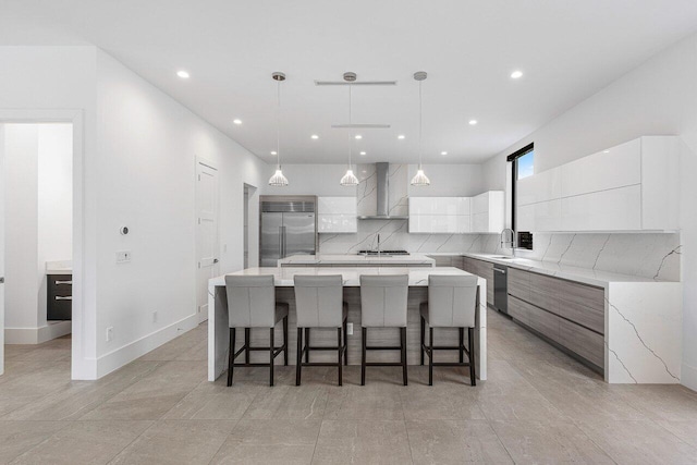 kitchen featuring stainless steel appliances, wall chimney range hood, a sink, modern cabinets, and a spacious island