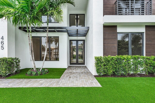 entrance to property featuring a balcony, french doors, and a yard