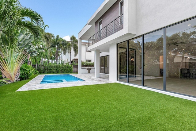 rear view of house featuring a balcony, a yard, a patio, a fenced in pool, and stucco siding