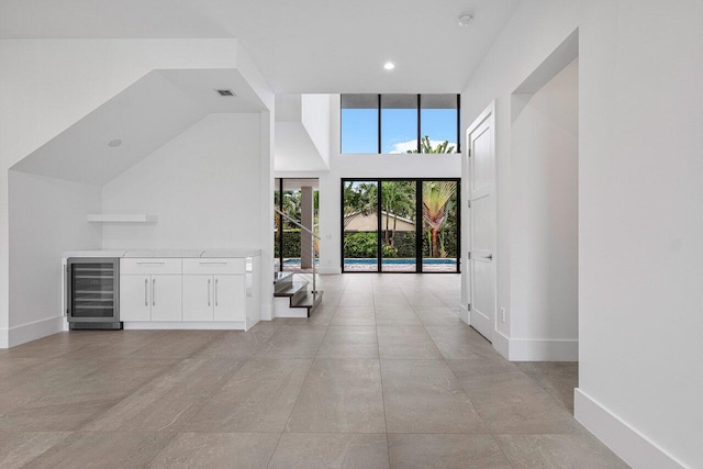 interior space with a towering ceiling, baseboards, visible vents, recessed lighting, and beverage cooler