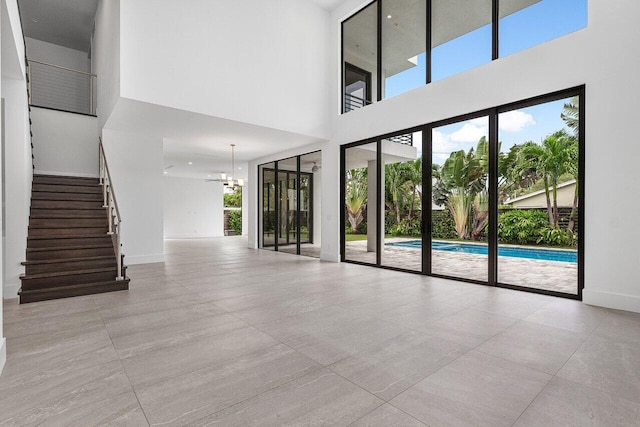 unfurnished living room featuring baseboards, a towering ceiling, stairs, and an inviting chandelier
