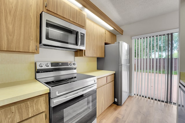 kitchen featuring stainless steel appliances, light hardwood / wood-style flooring, a textured ceiling, and light brown cabinets