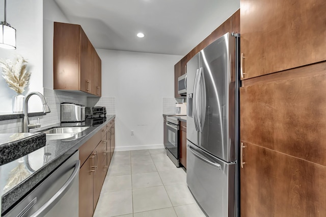 kitchen featuring a sink, dark stone counters, appliances with stainless steel finishes, light tile patterned floors, and decorative backsplash