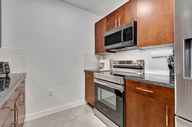 kitchen with dark stone counters, stainless steel appliances, light tile patterned floors, and tasteful backsplash