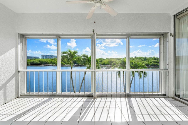 unfurnished sunroom with a healthy amount of sunlight, ceiling fan, and a water view