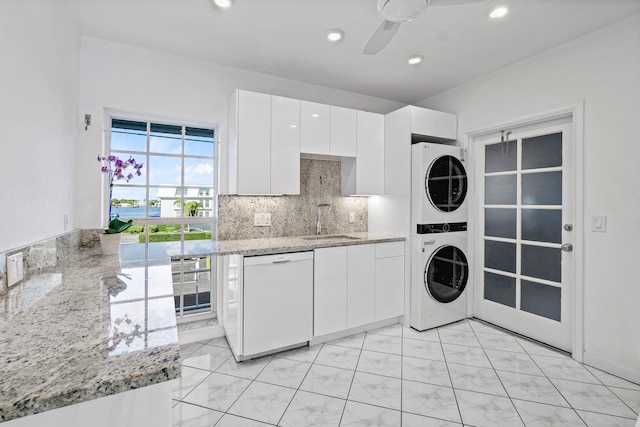 interior space featuring dishwasher, light stone counters, stacked washer and dryer, and white cabinets