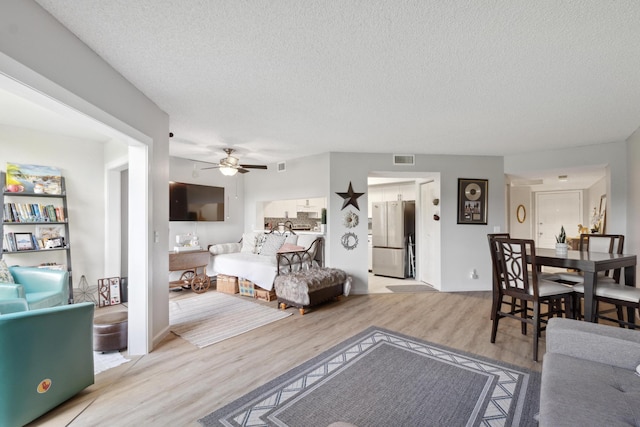 bedroom with ceiling fan, stainless steel fridge, a textured ceiling, and light wood-type flooring