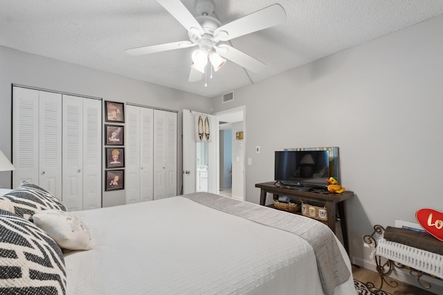 bedroom featuring hardwood / wood-style floors, two closets, a textured ceiling, and ceiling fan