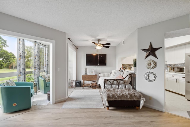 bedroom with connected bathroom, stainless steel refrigerator, ceiling fan, a textured ceiling, and light wood-type flooring