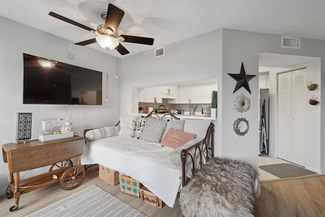 living room with ceiling fan, a textured ceiling, and light wood-type flooring