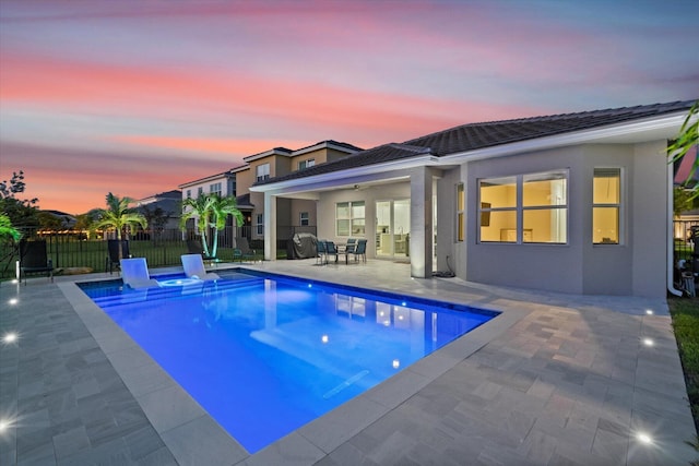 pool at dusk with a hot tub and a patio