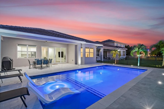 pool at dusk with ceiling fan, a hot tub, and a patio area