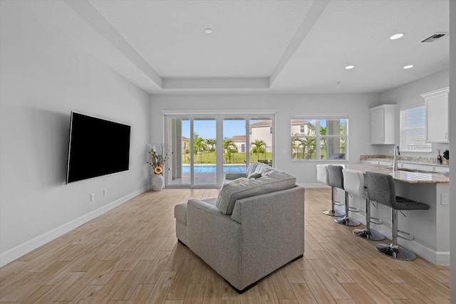 living room featuring a tray ceiling and sink