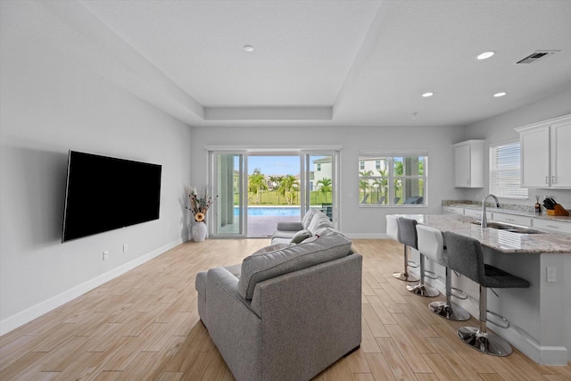 living room featuring a tray ceiling and sink