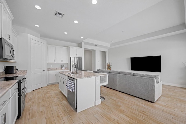 kitchen with white cabinets, a kitchen island with sink, light stone countertops, and stainless steel appliances