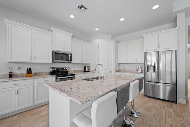 kitchen featuring white cabinetry, sink, stainless steel appliances, and a center island with sink