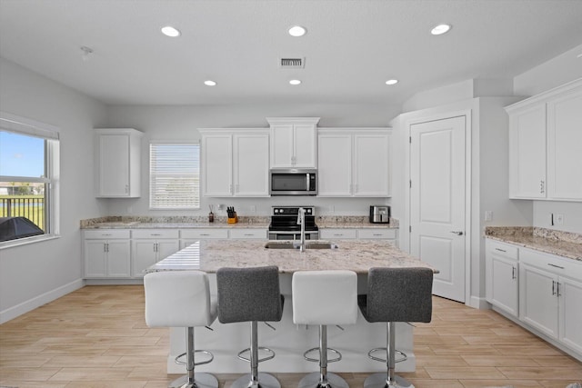 kitchen featuring light stone countertops, appliances with stainless steel finishes, white cabinets, and an island with sink