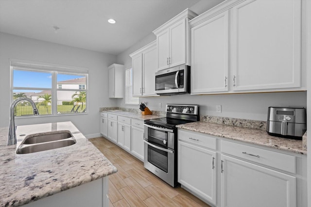 kitchen with light stone counters, sink, white cabinetry, and stainless steel appliances