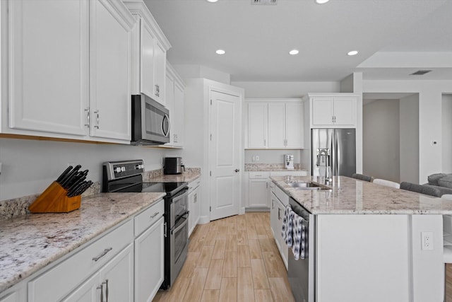 kitchen featuring appliances with stainless steel finishes, an island with sink, white cabinetry, and light hardwood / wood-style floors