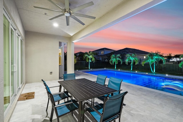 pool at dusk featuring ceiling fan and a patio