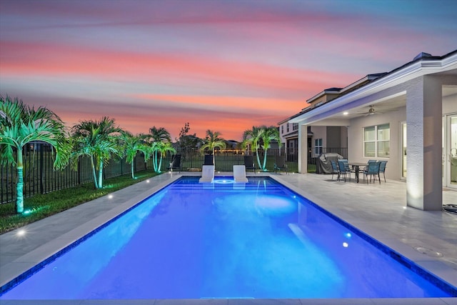 pool at dusk featuring ceiling fan and a patio