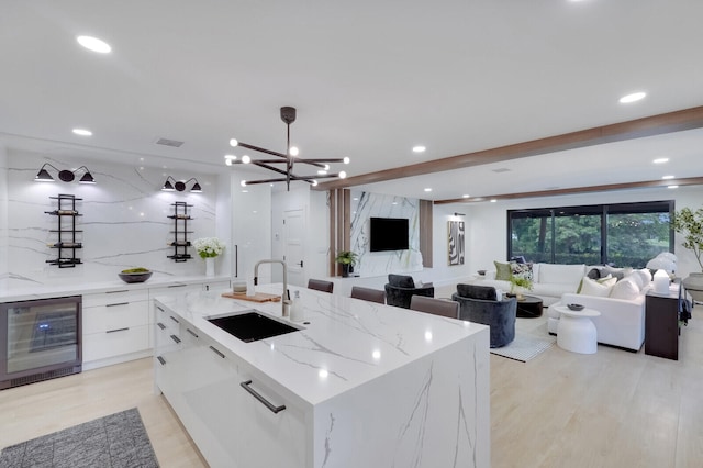 kitchen with light hardwood / wood-style flooring, white cabinetry, sink, an island with sink, and wine cooler