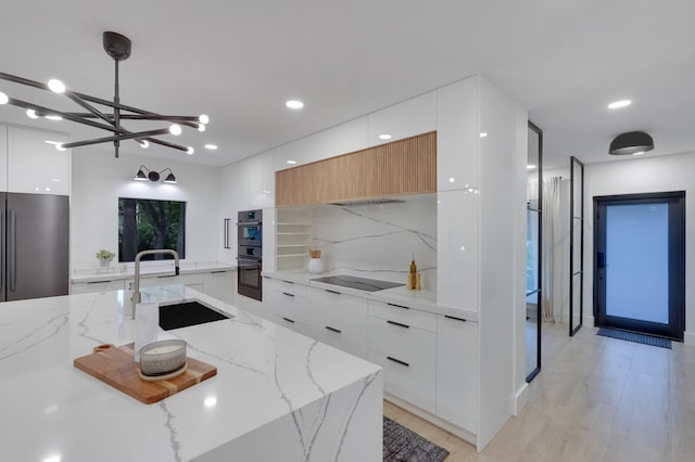 kitchen featuring decorative light fixtures, black appliances, sink, white cabinets, and light hardwood / wood-style floors