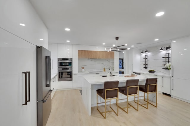 kitchen featuring light wood-type flooring, light stone countertops, stainless steel appliances, and white cabinetry