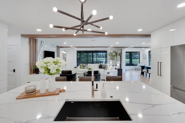 kitchen featuring stainless steel fridge, sink, light stone counters, light wood-type flooring, and white cabinets