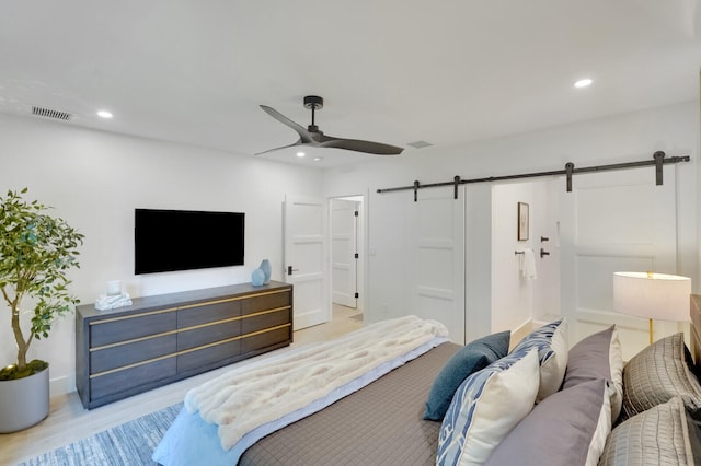 bedroom with light wood-type flooring, ceiling fan, and a barn door