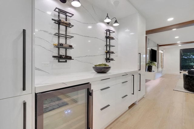 bar with light hardwood / wood-style flooring, light stone counters, white cabinetry, wine cooler, and beam ceiling