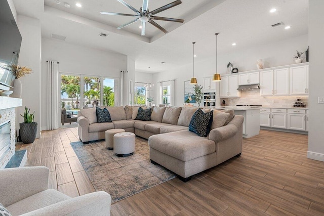 living room with a fireplace, light wood-type flooring, ceiling fan with notable chandelier, a tray ceiling, and a towering ceiling