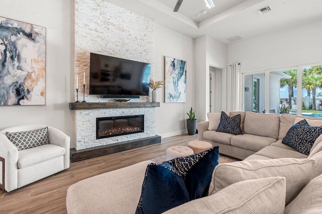 living room with hardwood / wood-style flooring, ceiling fan, and a stone fireplace