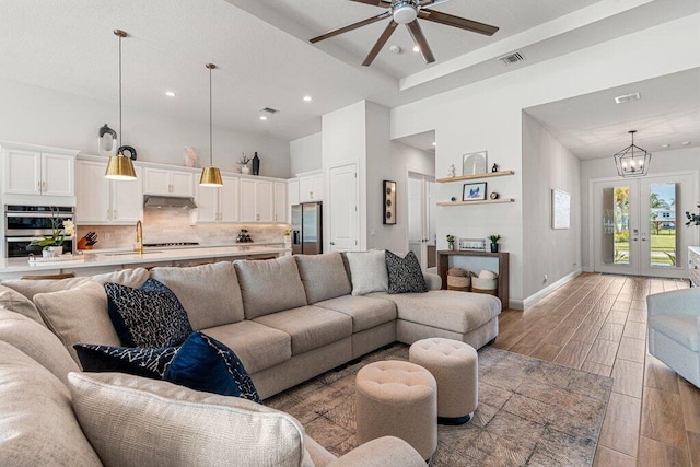 living room with a high ceiling, french doors, ceiling fan with notable chandelier, and light hardwood / wood-style flooring