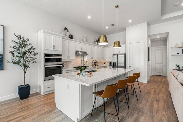 kitchen featuring a kitchen island with sink, white cabinetry, a kitchen bar, stainless steel appliances, and light hardwood / wood-style floors