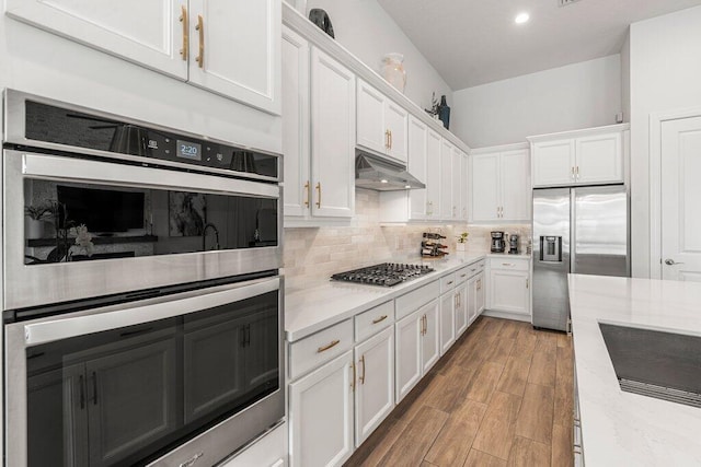 kitchen with appliances with stainless steel finishes, light stone counters, light hardwood / wood-style floors, white cabinetry, and decorative backsplash