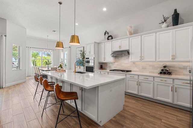 kitchen with hanging light fixtures, light wood-type flooring, gas stovetop, white cabinetry, and a center island with sink