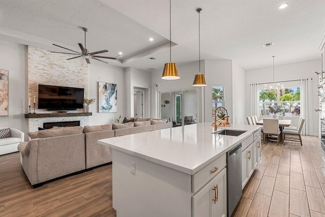 kitchen featuring light wood-type flooring, ceiling fan with notable chandelier, sink, a stone fireplace, and a center island with sink