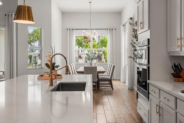 kitchen featuring light hardwood / wood-style flooring, hanging light fixtures, sink, stainless steel oven, and light stone counters