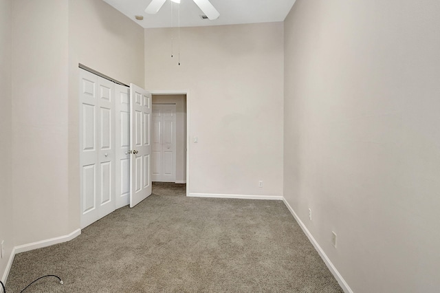 unfurnished bedroom featuring a towering ceiling, a closet, carpet flooring, and ceiling fan