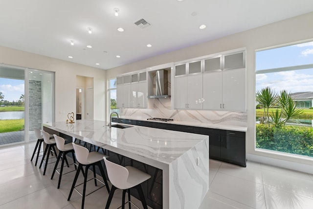 kitchen with plenty of natural light, stainless steel gas cooktop, wall chimney range hood, and white cabinetry