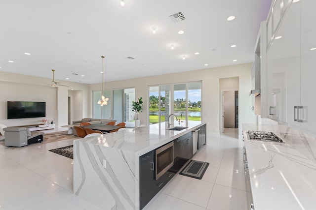 kitchen with white cabinets, light stone countertops, stainless steel appliances, sink, and a spacious island