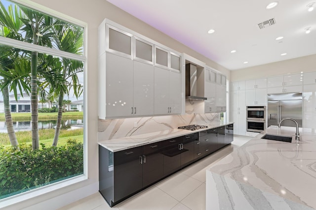 kitchen with wall chimney exhaust hood, appliances with stainless steel finishes, sink, and white cabinets