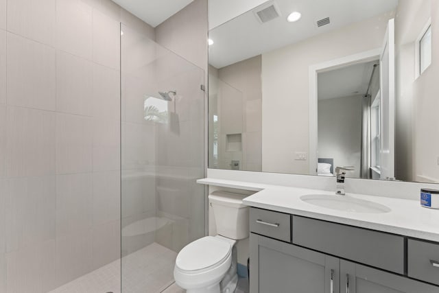 bathroom with tiled shower, vanity, and toilet