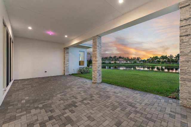 patio terrace at dusk featuring a yard and a water view