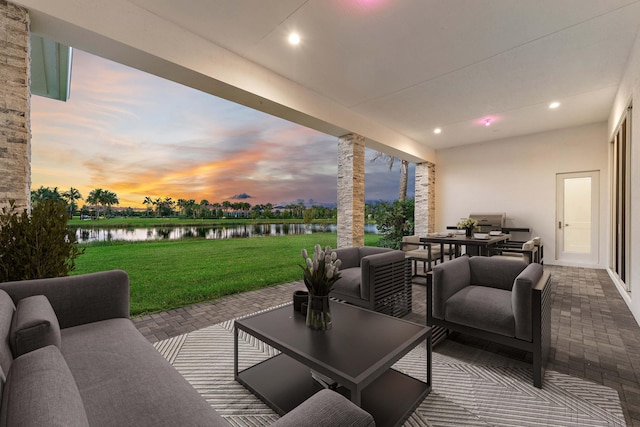 patio terrace at dusk featuring a water view and a lawn