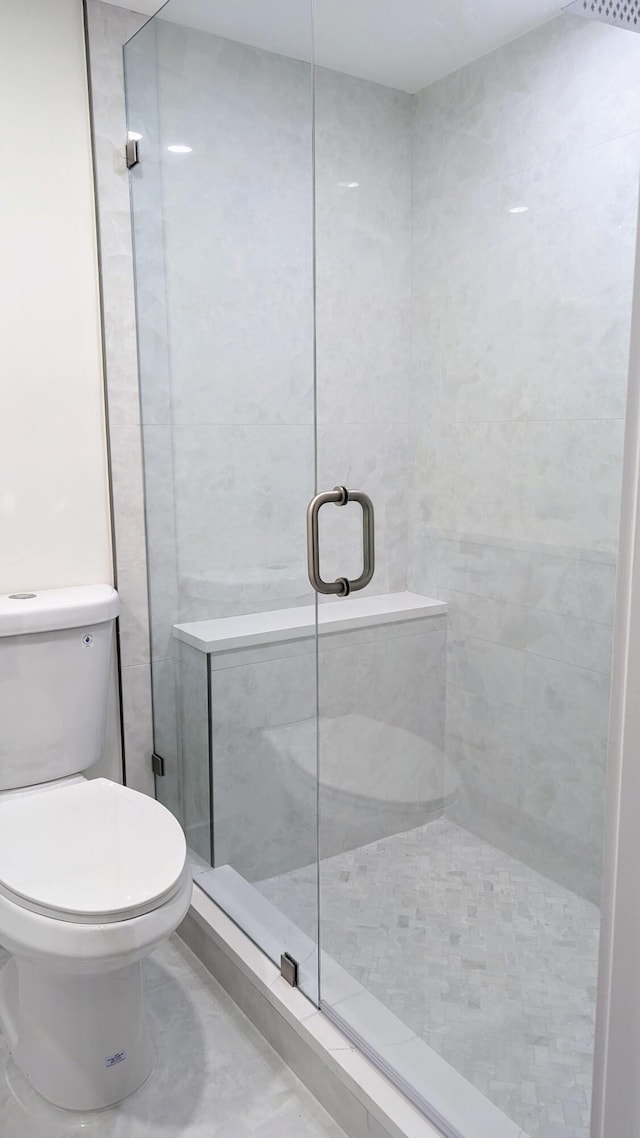 bathroom featuring tile patterned floors, a shower with door, tile walls, and toilet