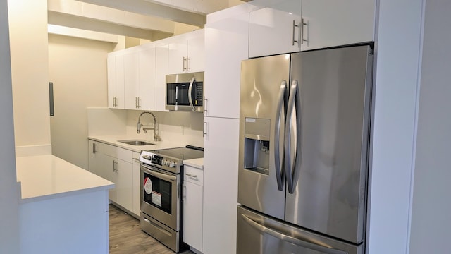 kitchen with sink, beamed ceiling, appliances with stainless steel finishes, light hardwood / wood-style floors, and white cabinets